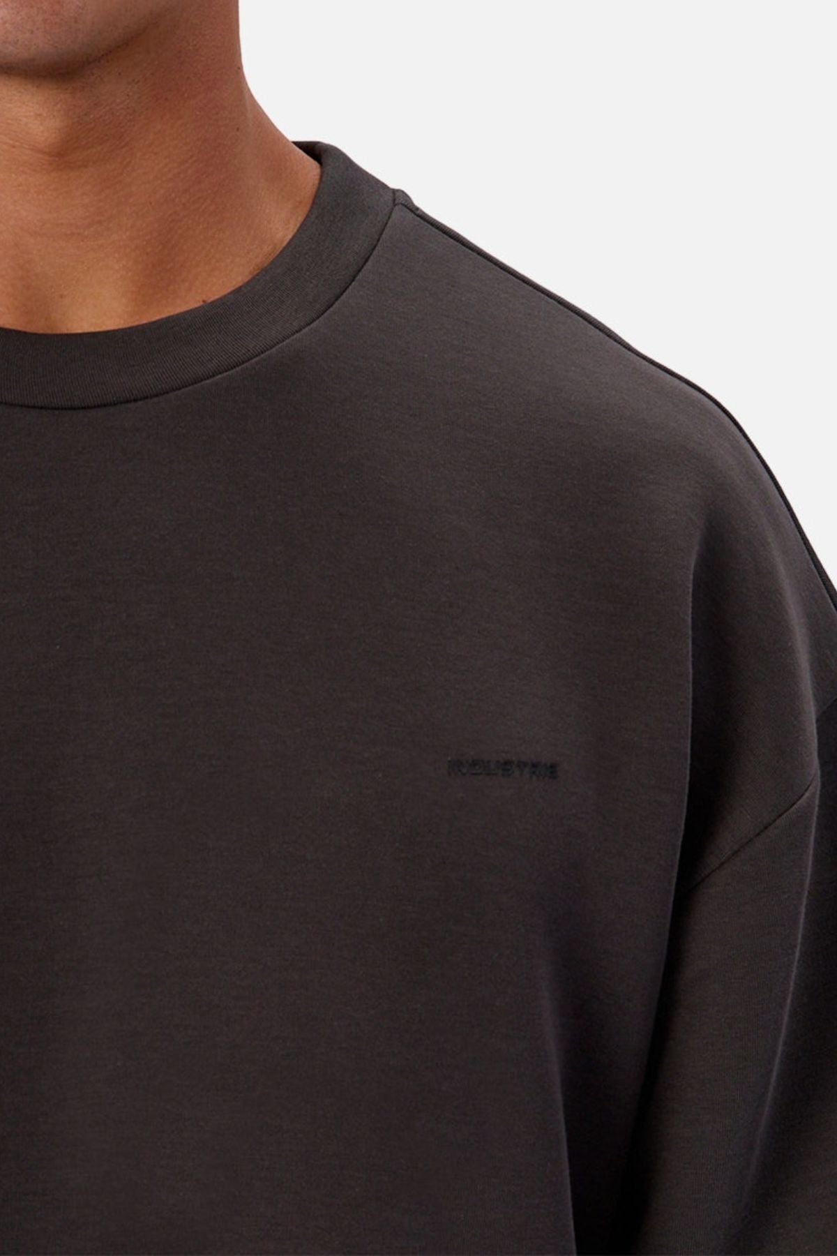 A close-up of someone in the Industrie The Tech Del Sur Sweat, an athletic sweatshirt with a round neckline and subtle βKOLLEKTIVβ embroidery on the left chest in matching dark thread. The background is neutral.