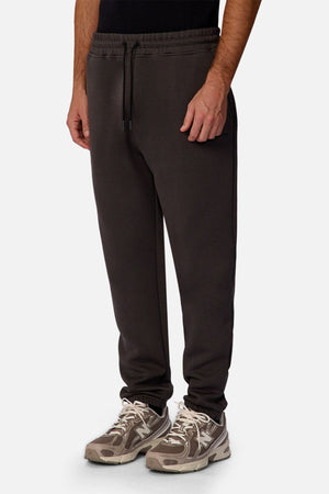 A person wearing Industrie The Tech Del Sur Track Pant in black and beige athletic sneakers stands against a plain white background, with only the lower half of their body visible.