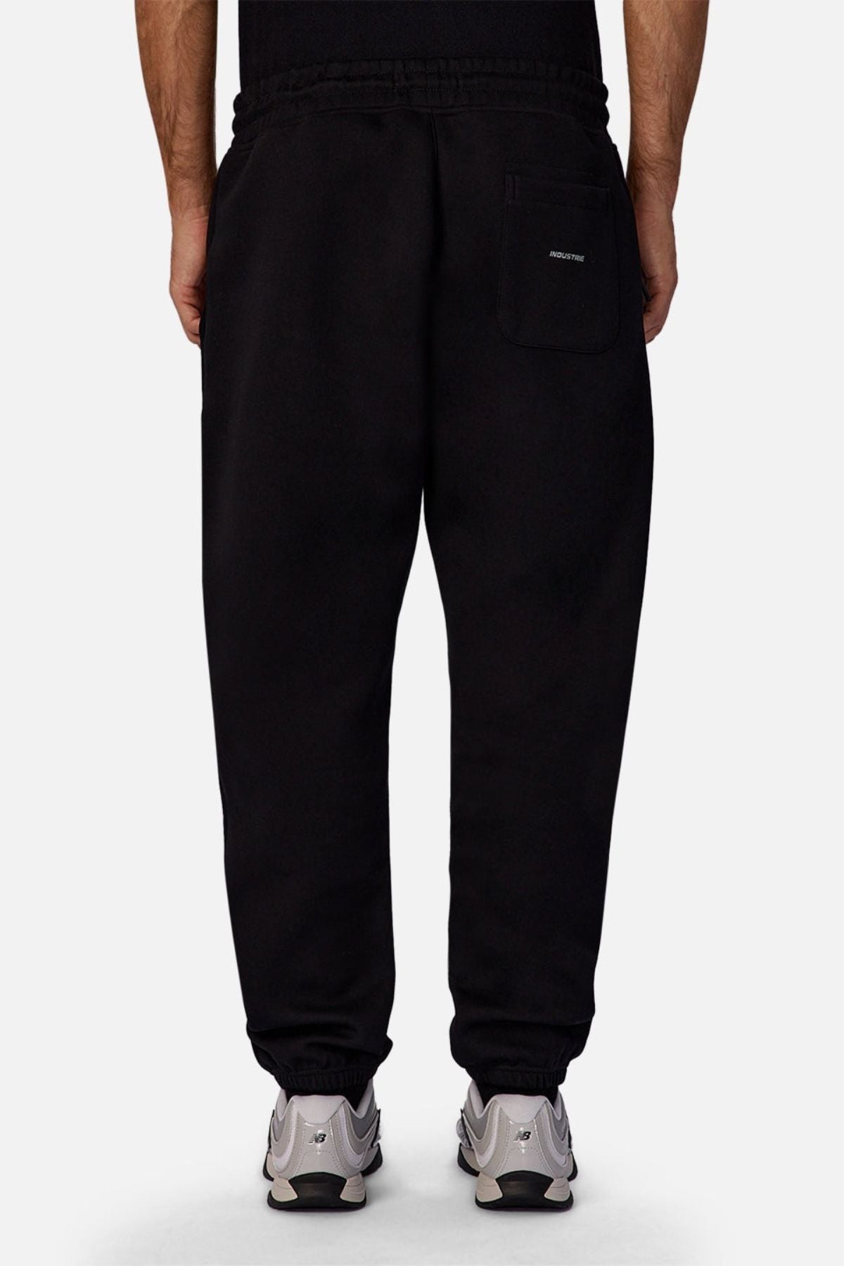 A person is seen from behind wearing Industrie The Tech Del Sur Track Pant in black, featuring an elastic waistband, elastic cuffs, and a single right-side patch pocket, paired with white sneakers.