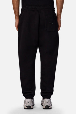 A person is seen from behind wearing Industrie The Tech Del Sur Track Pant in black, featuring an elastic waistband, elastic cuffs, and a single right-side patch pocket, paired with white sneakers.