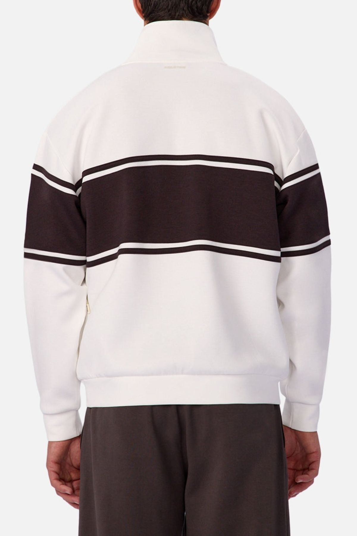 Someone wears the Industrie The Tech Southend Track Top, a white jacket with wide dark stripes on the back and arms, paired with dark pants and photographed from behind against a plain background for a relaxed, casual style.
