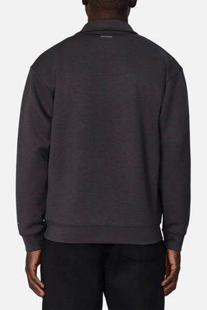A person is shown from the back wearing Industrie The Zip Thru Track Top in dark gray and black pants. The soft, trendy fabric of the track top features a small text logo near the neckline and offers a relaxed fit. The plain white background highlights its understated athletic style.