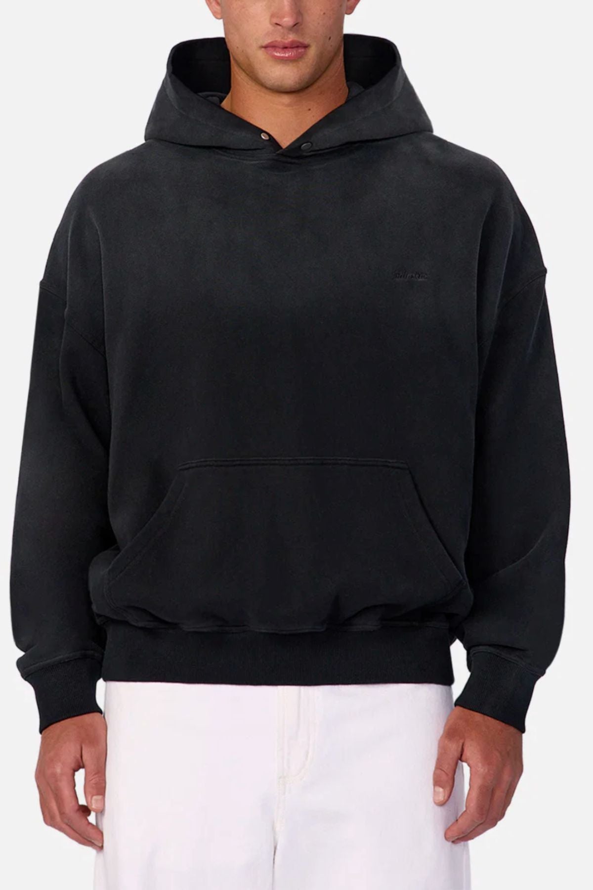 Someone wearing the Industrie The Sandblast Hoodie in black—made from 100% cotton and featuring a front pocket—paired with white pants stands against a simple light gray background, creating an effortlessly laid-back look.