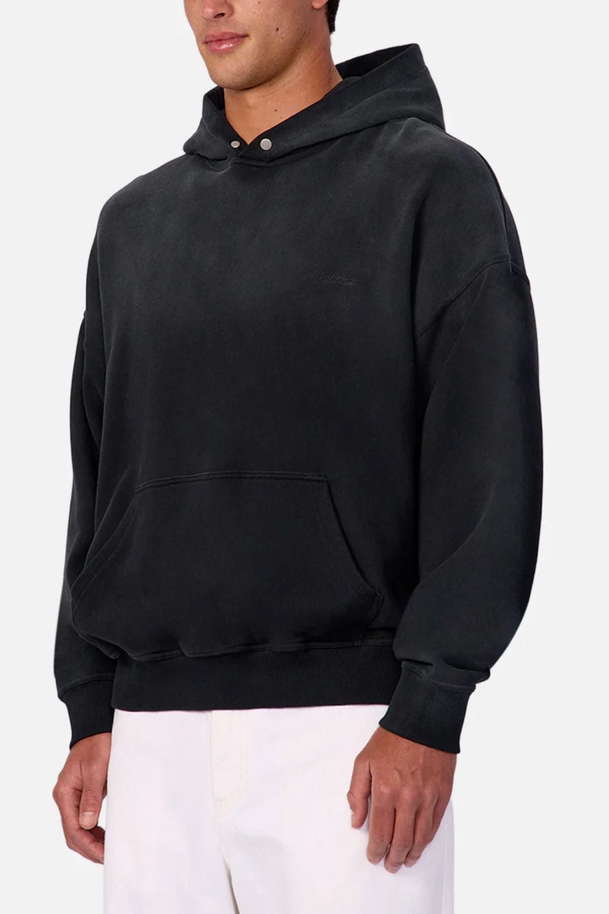 With a relaxed vibe, a person wearing the Industrie The Sandblast Hoodie—100% cotton with a front pocket—and white pants stands against a plain light gray background. Their face is partially out of frame.