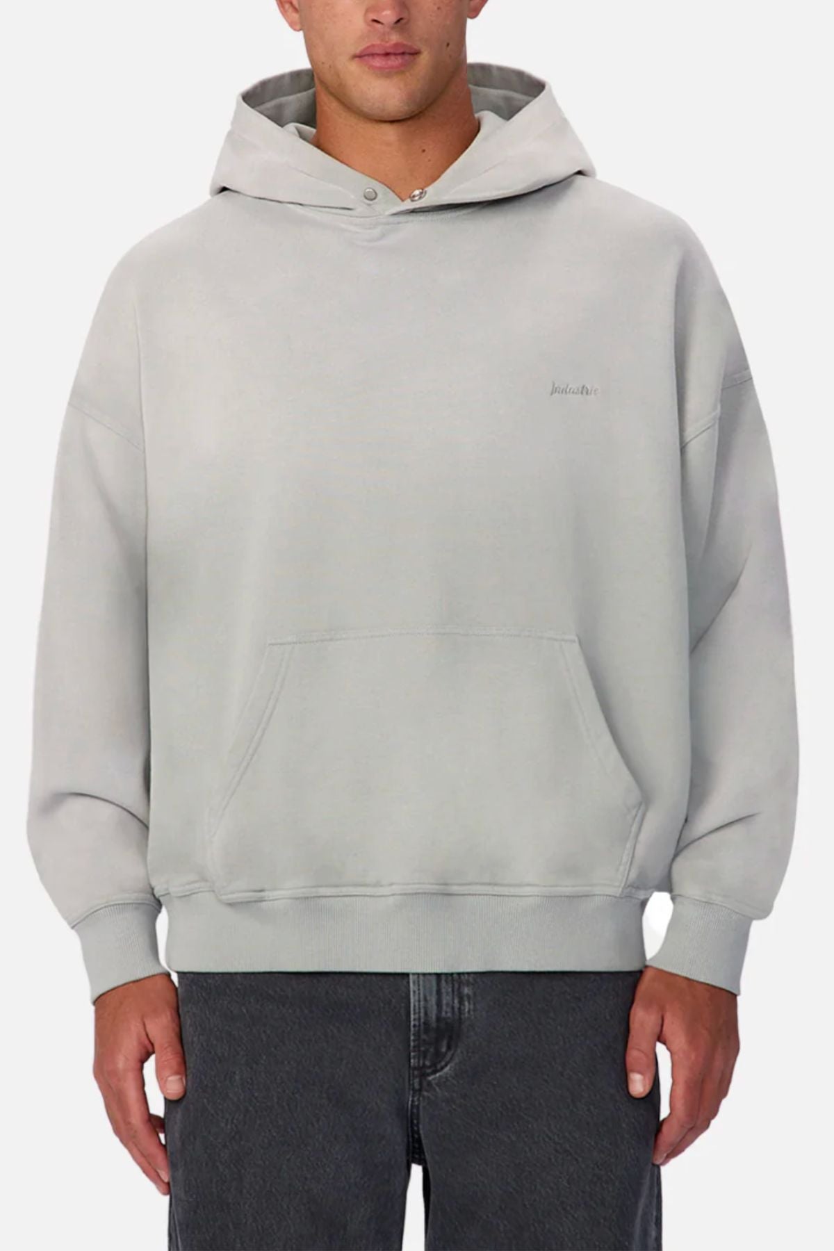 Wearing the Industrie The Sandblast Hoodie in light gray with a front pocket and hood, paired with dark gray jeans, this person shows off a relaxed look against a plain white background.
