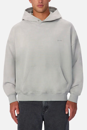 Wearing the Industrie The Sandblast Hoodie in light gray with a front pocket and hood, paired with dark gray jeans, this person shows off a relaxed look against a plain white background.