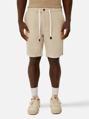 A person is wearing a pair of Industrie The Baller Linen Shorts in beige, featuring a knee-length fit with a drawstring waist and front button closure. They are also sporting white socks and fashionable sneakers with a multi-colored design. The image highlights the individual's ensemble from the waist down, perfectly showcasing the knee-length style of the Industrie The Baller Linen Shorts.