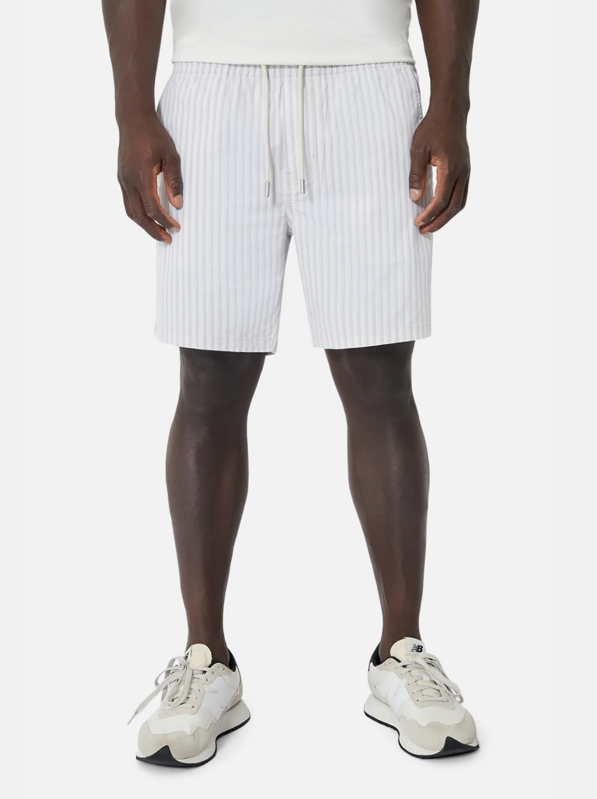 Front view of a person wearing Industrie The Marchena Bahama Short, featuring light gray vertical stripes and an elastic waist, paired with white sneakers. Hands at their sides, they capture the relaxed summer vibe against a plain white background.