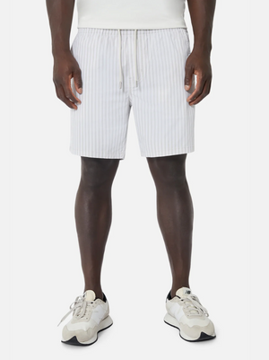 Front view of a person wearing Industrie The Marchena Bahama Short, featuring light gray vertical stripes and an elastic waist, paired with white sneakers. Hands at their sides, they capture the relaxed summer vibe against a plain white background.