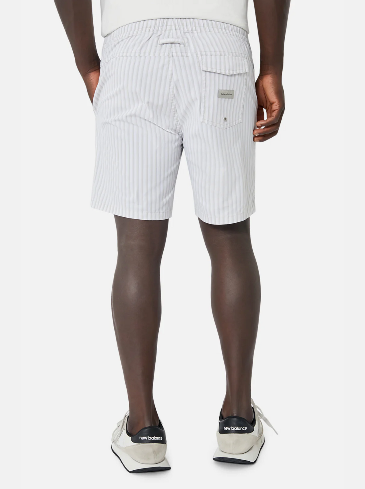 A person is seen from behind sporting Industrie The Marchena Bahama Short in light gray stripes with an elastic waist, paired with a white shirt and white sneakers featuring black soles. This ensemble is ideal for relaxed summer days, standing out elegantly against the plain white background.