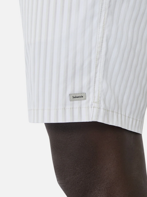 Close-up of a person wearing Industrie The Marchena Bahama Short, featuring white fabric with vertical light gray stripes and an elastic waist for comfort. A small rectangular "Industrie" tag is on the lower side, perfect for summer days against a plain white background.