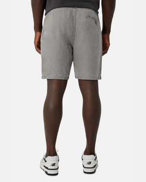A person is seen from behind wearing gray denim shorts with pockets, similar in style to Industrie The Marina Linen Short, and white sneakers with black accents against a crisp white background.