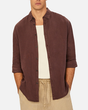 A person wears an Industrie The Tennyson Linen Shirt, unbuttoned over a beige tank top, with classic rolled-up sleeves. Their hands rest in the pockets of beige pants against a plain white background.