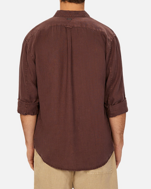 A person with their back to the camera wears Industrie The Tennyson Linen Shirt, a long-sleeved, classic-style, 100% pure linen brown shirt with rolled-up sleeves and a relaxed fit, paired with light beige pants against a plain background.