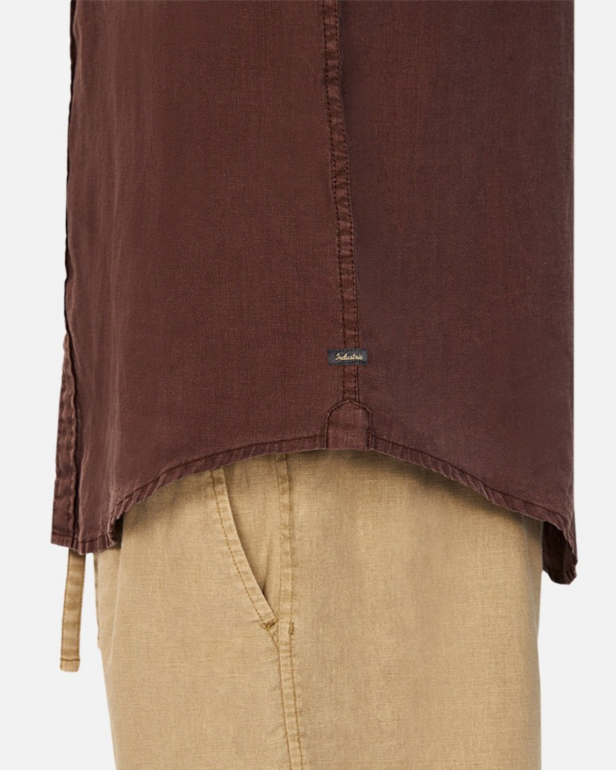 Close-up of a person wearing Industrie The Tennyson Linen Shirt in classic brown and beige pants. The 100% pure linen shirt features a small tag near the hem, focusing on textures and colors against a plain background.