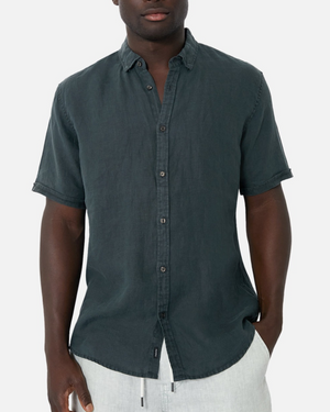 A man wears the Industrie The Tennyson Linen Short Sleeve Shirt with light-colored drawstring pants, standing hands-in-pockets against a white background for a smart-casual look.