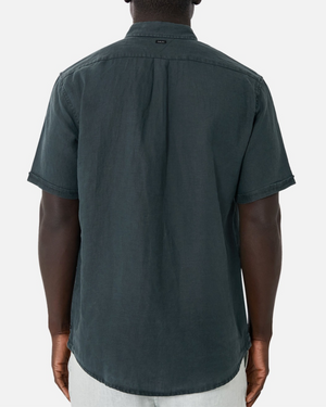 Someone seen from behind wears the Industrie The Tennyson Linen Short Sleeve Shirt in dark linen with light-colored pants, standing against a plain white background.