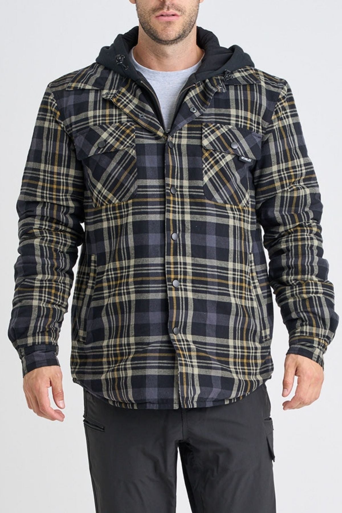 A man wearing a Jetpilot Quilted Flannel Jacket in black, gray, and yellow plaid over a gray shirt. The cotton jacket features front buttons and chest pockets. He pairs it with black pants, and his face is partially visible.