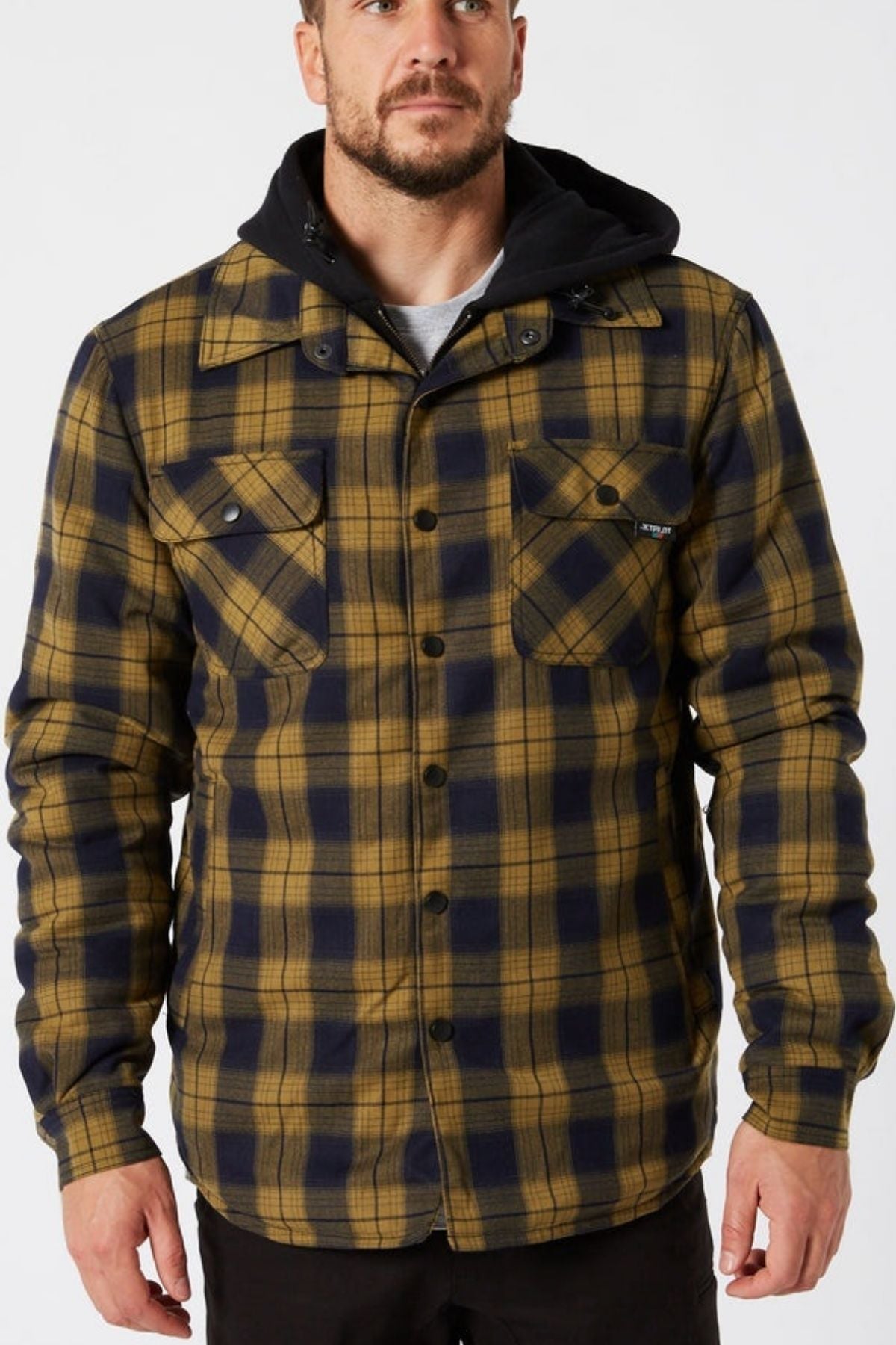 A man wears a Jetpilot Quilted Flannel Jacket in yellow and navy blue over a black hoodie, standing forward with hands by his sides. The jacket features button closures and two chest pockets.