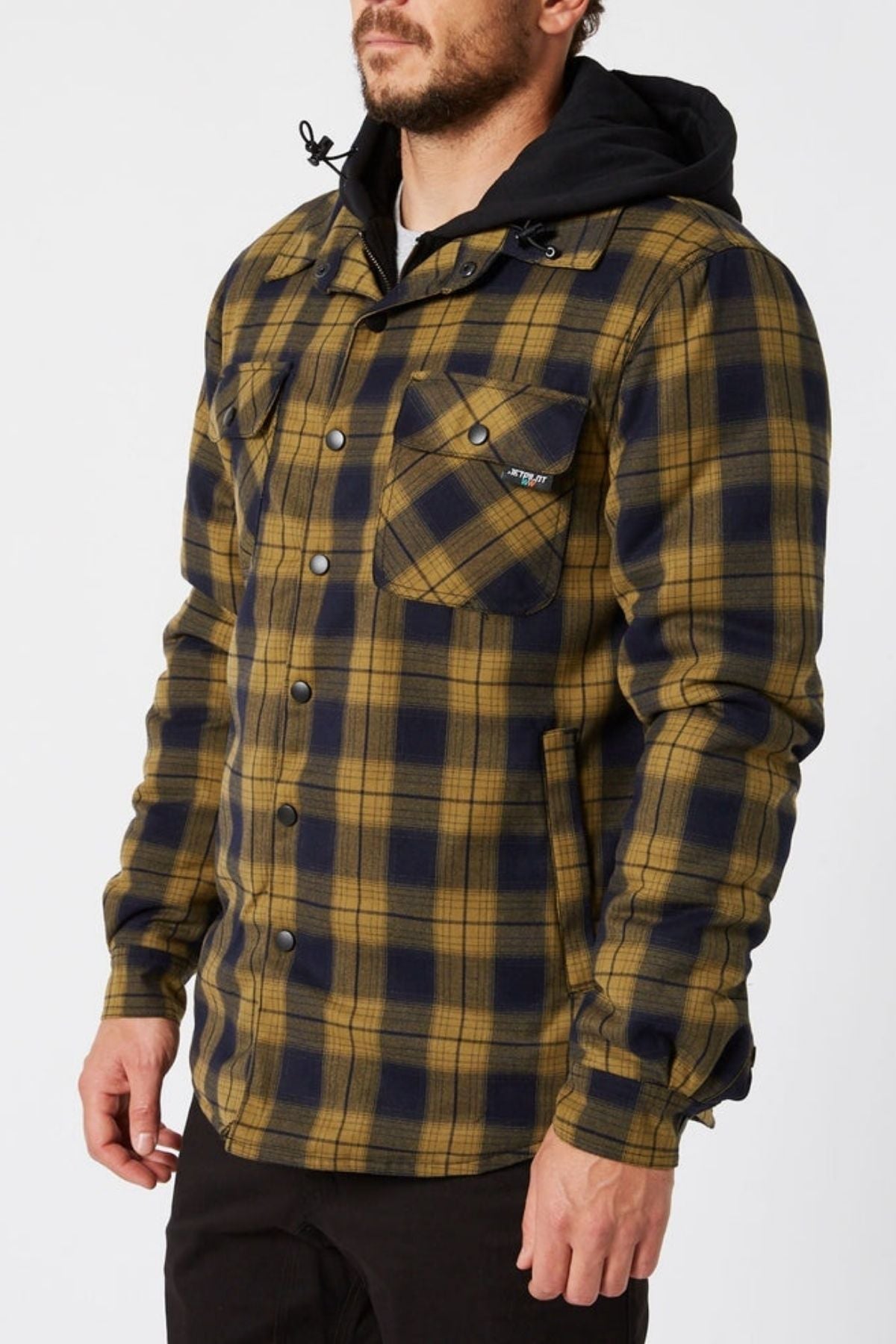 Man wearing a Jetpilot Quilted Flannel Jacket, featuring yellow and navy cotton flannel with a hood, paired with black pants and a black shirt, standing against a plain white background.
