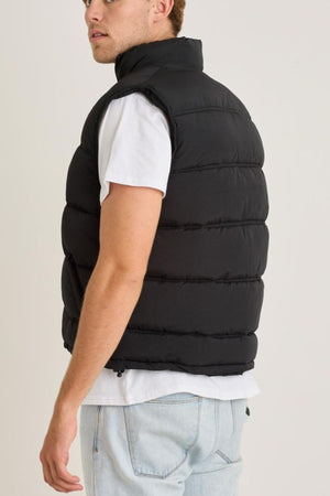 A person in a white T-shirt, light blue jeans, and the Jetpilot Zip Up Vest stands slightly turned away from the camera, glancing over their shoulder against a plain background.