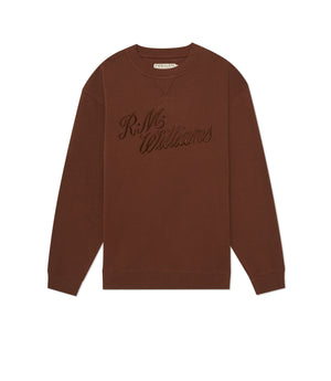 The RM Williams R.M.W Script Crew Neck is a brown cotton blend jumper with long sleeves, ribbed cuffs, and cursive R.M.Williams embroidery on the chest, shown laid flat on a white background.