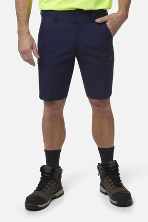 A person stands against a plain white background wearing King Gee Workcool Pro Shorts in navy, paired with a neon yellow shirt, black socks, and brown work boots. Only the lower half of their body is visible.