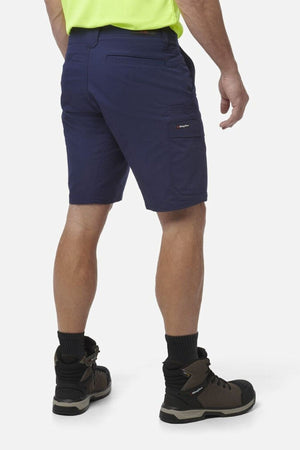 A person wearing King Gee Workcool Pro Shorts in navy blue, a neon yellow shirt, black socks, and brown work boots stands with their back to the camera against a plain white background.