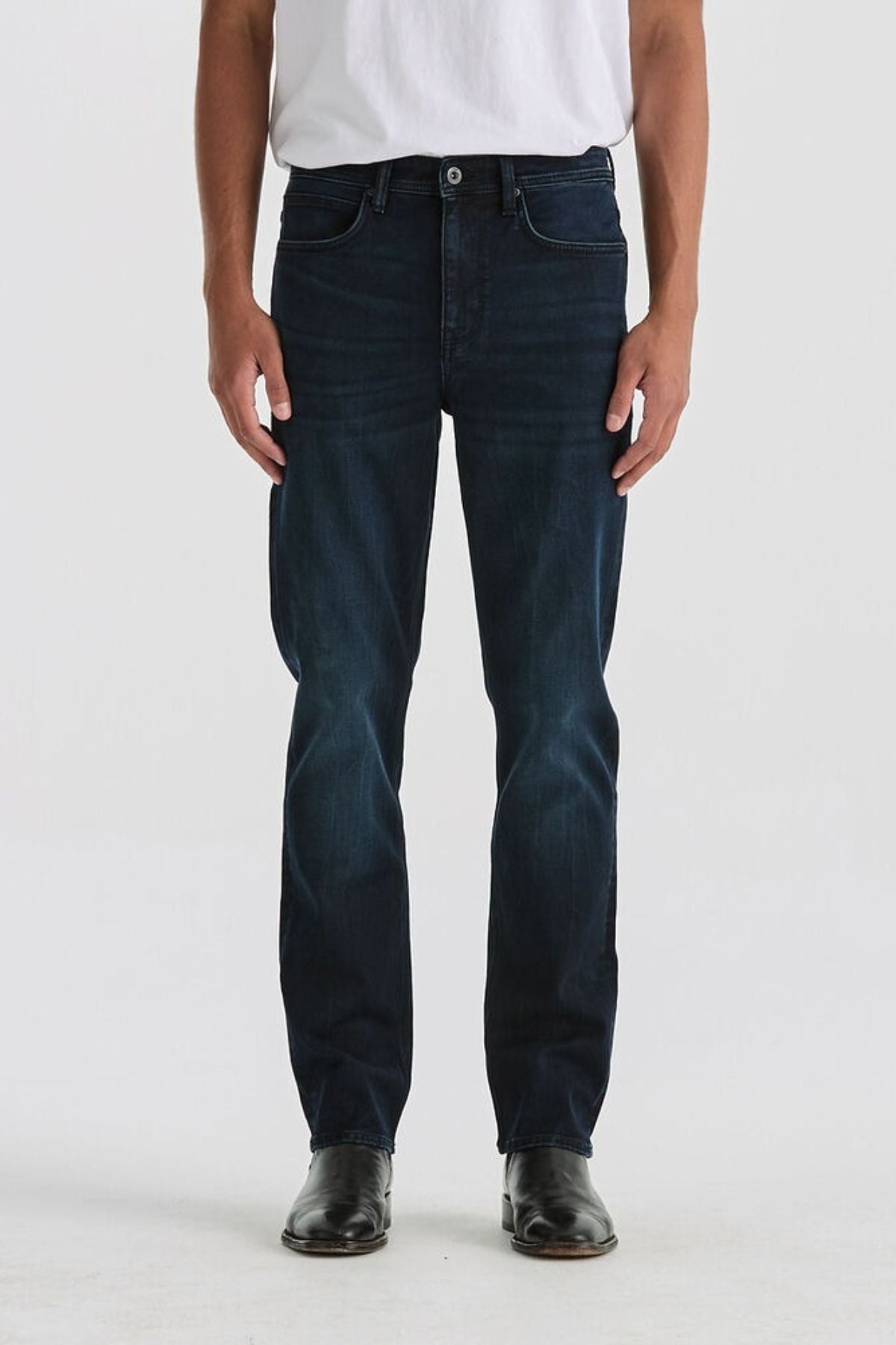 A person wearing a white t-shirt, Lee Originals L100 Slim Jean with a comfortable fit, and black shoes stands against a plain light background. The image is cropped from the shoulders down.