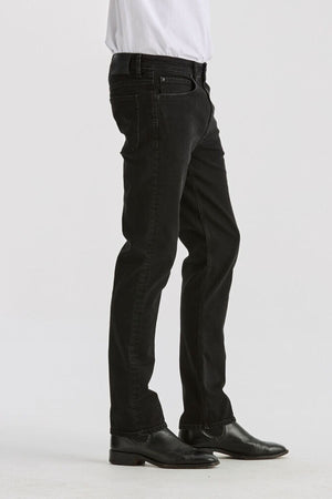 A person in a white shirt, Lee Originals L100 Slim Jean, and black dress shoes stands sideways against a plain white background—a look that embodies timeless style.