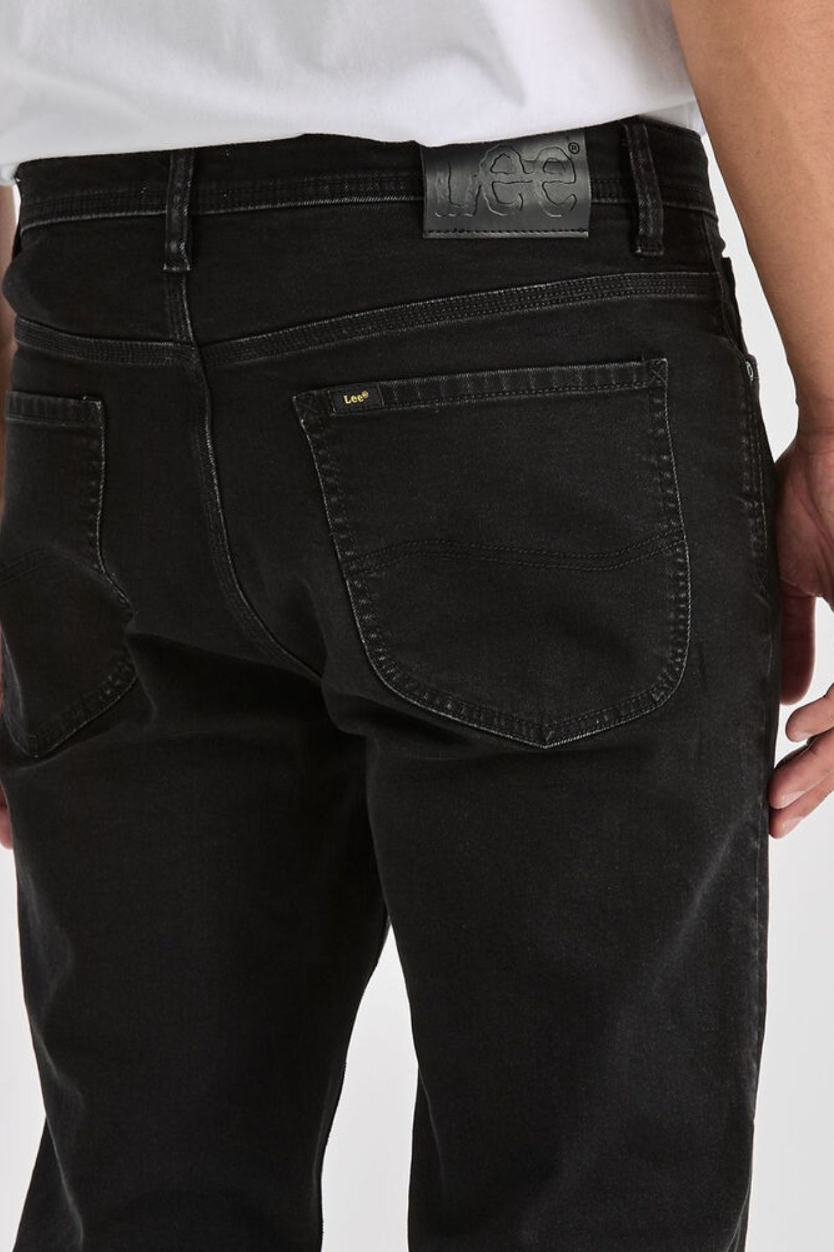 Close-up of a person wearing Lee Originals L100 Slim Jean with visible back pockets and a black leather Lee patch on the waistband. A white shirt tucked in highlights the timeless style of these jeans.