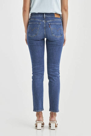 A person is shown from the back against a plain white background wearing Levis 312 Shaping Slim Jeans, which feature stretch fabric, two back pockets, and a light brown waistband patch, paired with white heeled sandals.