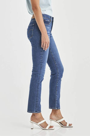 Wearing Levis 312 Shaping Slim Jean, a light blue top, and white heeled sandals, a person stands side-on against a plain white background with only the lower half of their body visible.