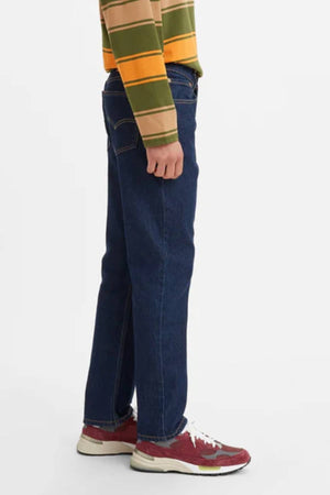 A person in a striped long-sleeve shirt, Levis 516 Straight Jean, and red sneakers stands sideways against a plain white background.