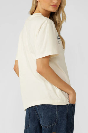 A woman with long blonde hair models the oversized Lorna Jane Active Living T-Shirt and dark blue jeans, standing sideways with one hand in her pocket against a plain backgroundโan effortless look for active living.