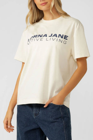 A woman wears the Lorna Jane Active Living T-Shirtโan oversized, premium cotton jersey with bold letteringโpaired with blue jeans, standing with one hand relaxed by her side.