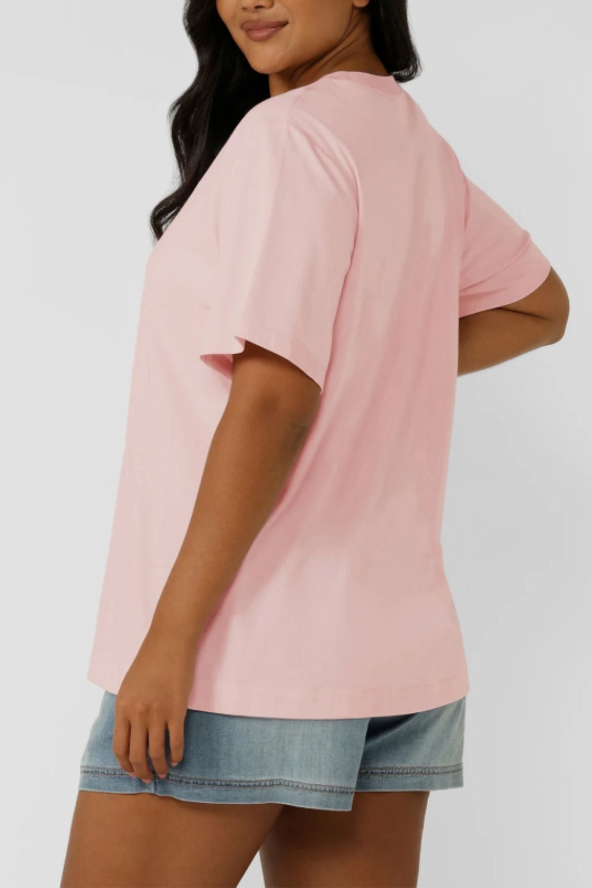 A woman stands sideways against a plain background wearing the Lorna Jane Chalet Relaxed T-Shirt and light blue denim shorts.