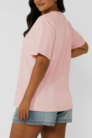 A woman stands sideways against a plain background wearing the Lorna Jane Chalet Relaxed T-Shirt and light blue denim shorts.
