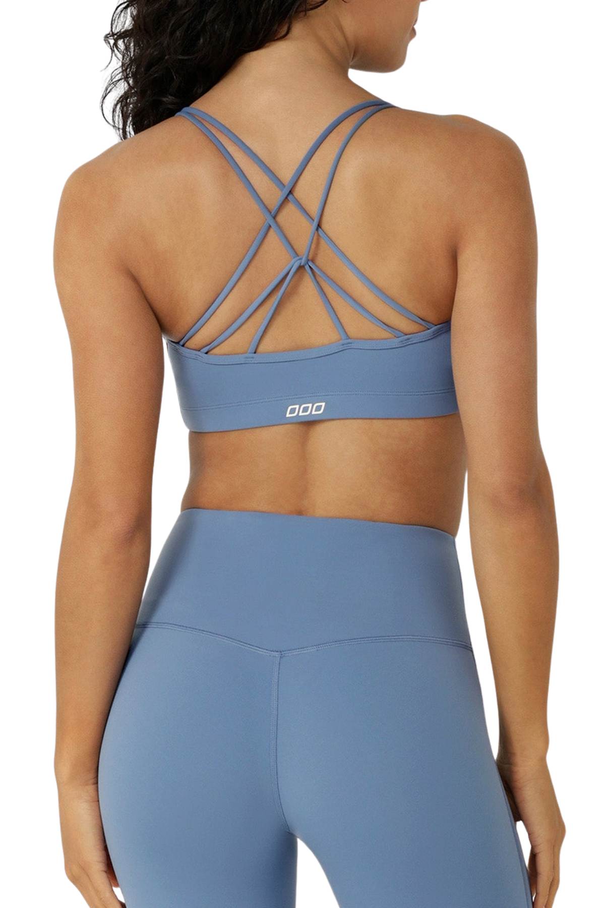 Woman wearing the Lorna Jane Lotus Cropped Sports Bra with crisscross straps and matching high-waisted leggings, shown from the back against a white background.