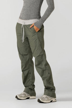 Someone stands with hands in pockets, wearing a fitted gray long-sleeve shirt and Lorna Jane Flashdance Pant with an adjustable waist, paired with white athletic shoes, against a plain light background.