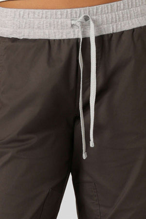 Close-up of a person wearing the Lorna Jane Flashdance Pant in brown, featuring an elastic waistband, light gray drawstring, and reinforced seams, shown from waist to upper thigh.