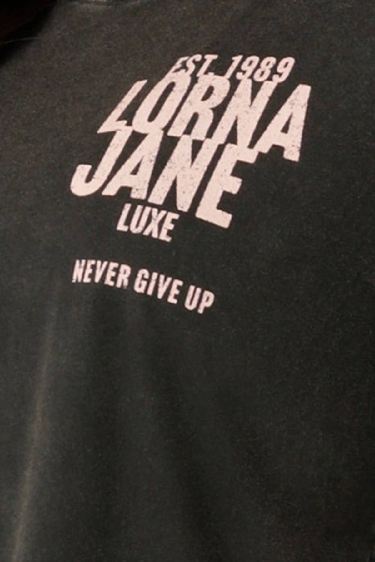 Close-up of a black Lorna Jane Heritage Inspiration Relaxed T-Shirt with vintage wash, featuring white text: "EST. 1989 LORNA JANE LUXE NEVER GIVE UP.
