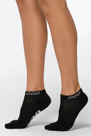 A person stands on tiptoe wearing Lorna Jane Iconic Socks with a white geometric design near the cuffs, set against a plain white background.