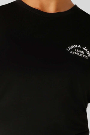 Close-up of a person wearing the Lorna Jane Lotus Muscle Tank, showing only the neck and upper torso. This black tank features “Lorna Jane Luxe Athletic” in white text on the chest, highlighting its lightweight design for easy layering.
