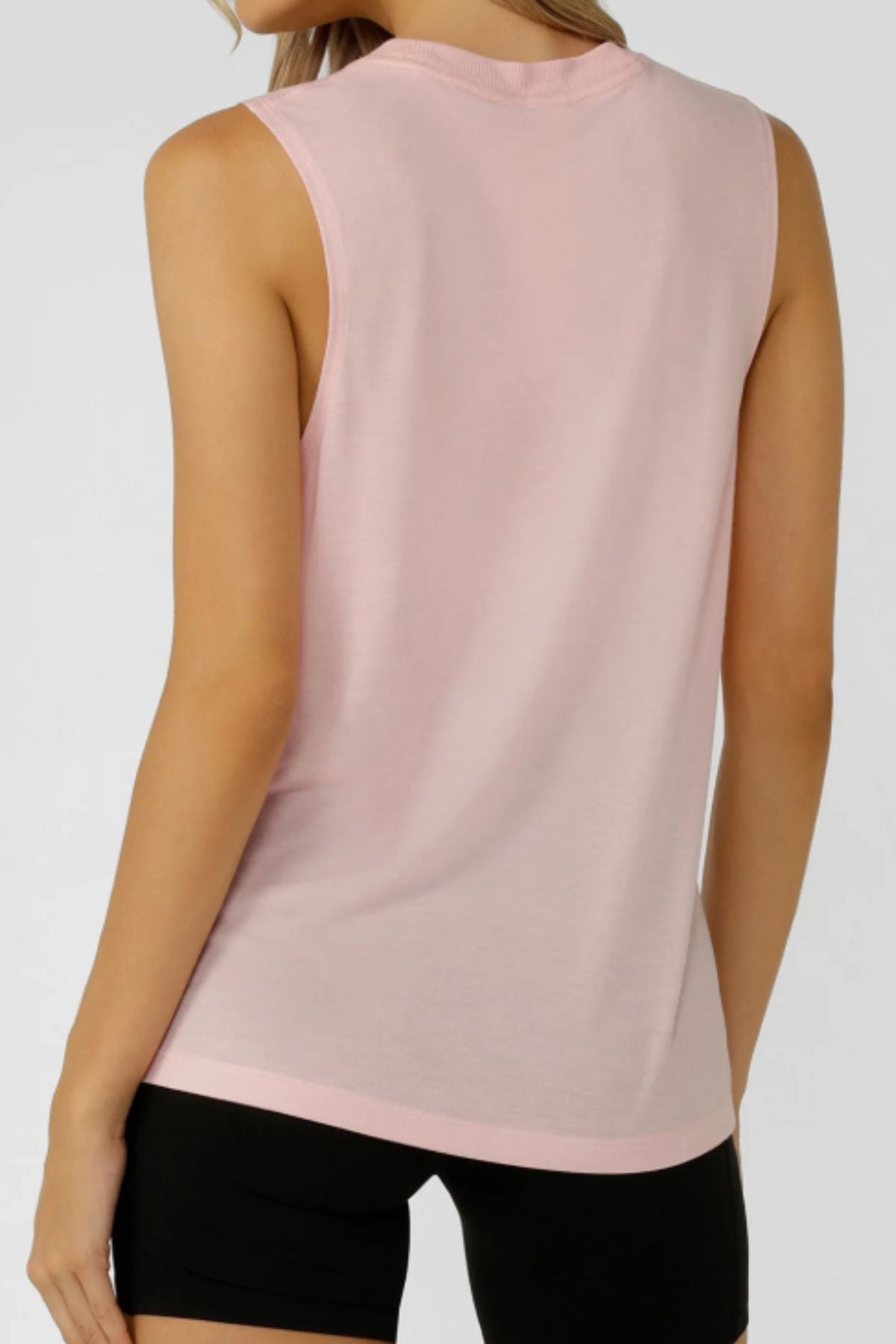 A woman with long blonde hair and light skin is shown from the back wearing the Lorna Jane Lotus Muscle Tank in light pink and black shorts, set against a plain, neutral background.