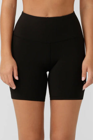 A person wears Lorna Jane Lotus No Chafe Phone Pocket 12cm Bike Shorts in black, shown from waist to mid-thigh against a plain light background.