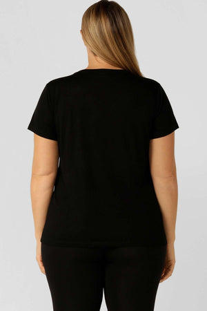 A person with light brown hair is seen from behind wearing a plain black Lorna Jane Lotus T-Shirt and black pants, standing against a plain light gray background.