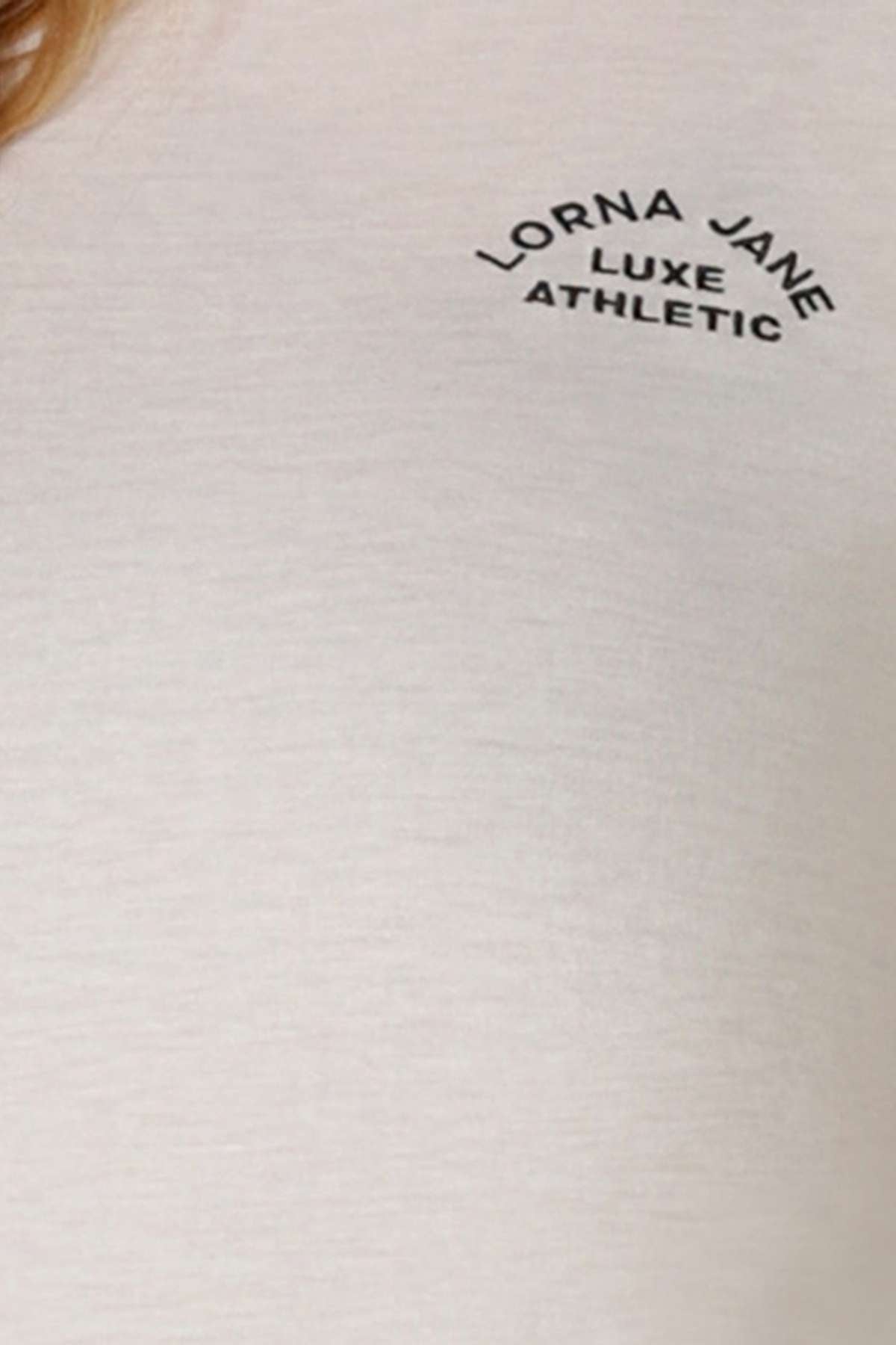 Close-up of a light-colored Lorna Jane Lotus T-Shirt featuring "LORNA JANE LUXE ATHLETIC" in black above the left chest—ideal for an active lifestyle.
