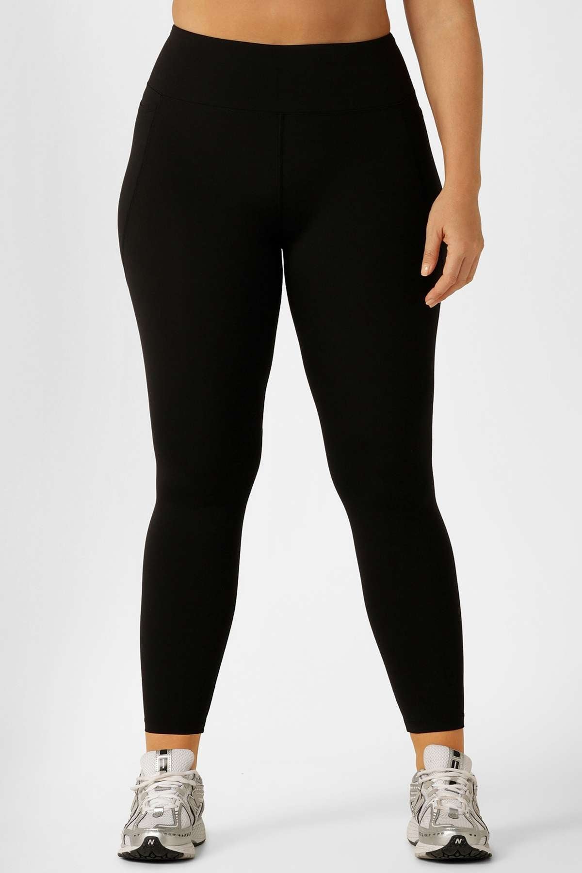 A person wears Lorna Jane Lotus Thermal No Chafe Full Length Leggings in black with white sneakers, standing against a plain white background. Only the lower torso and legs are visible.