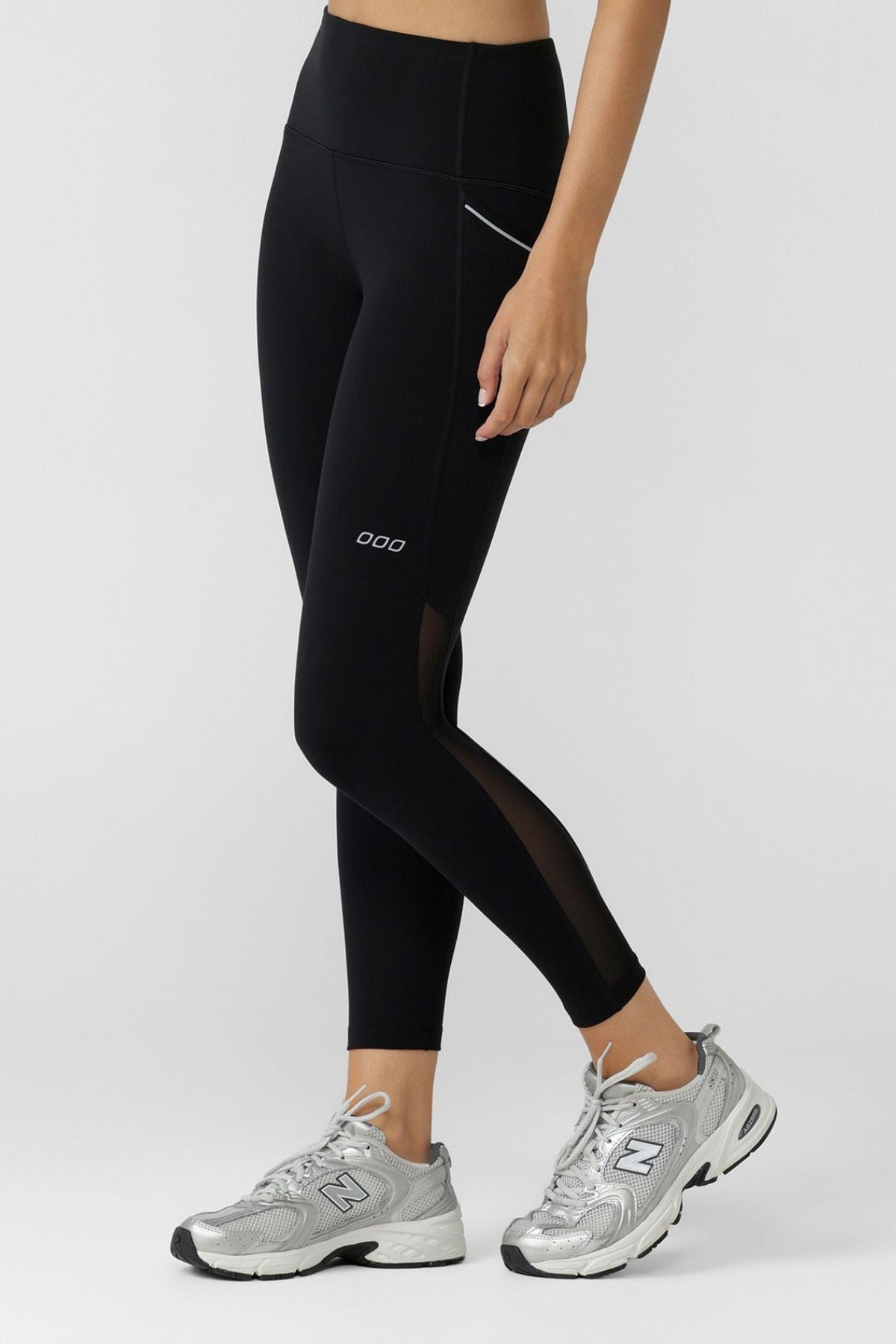 Only the lower body is visible as a person wearing Lorna Jane Peak Performance 3 Pocket Ankle Biter Leggings and gray athletic sneakers stands against a plain light gray background.